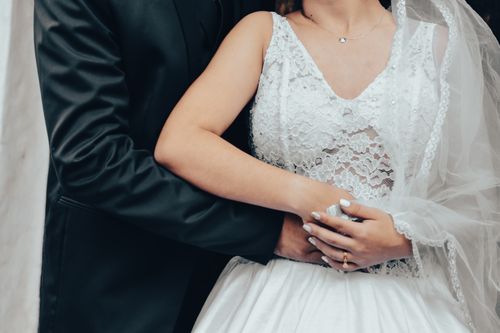 Free Close-up of a bride and groom in formal attire, highlighting a lace wedding dress and black tuxedo. Stock Photo