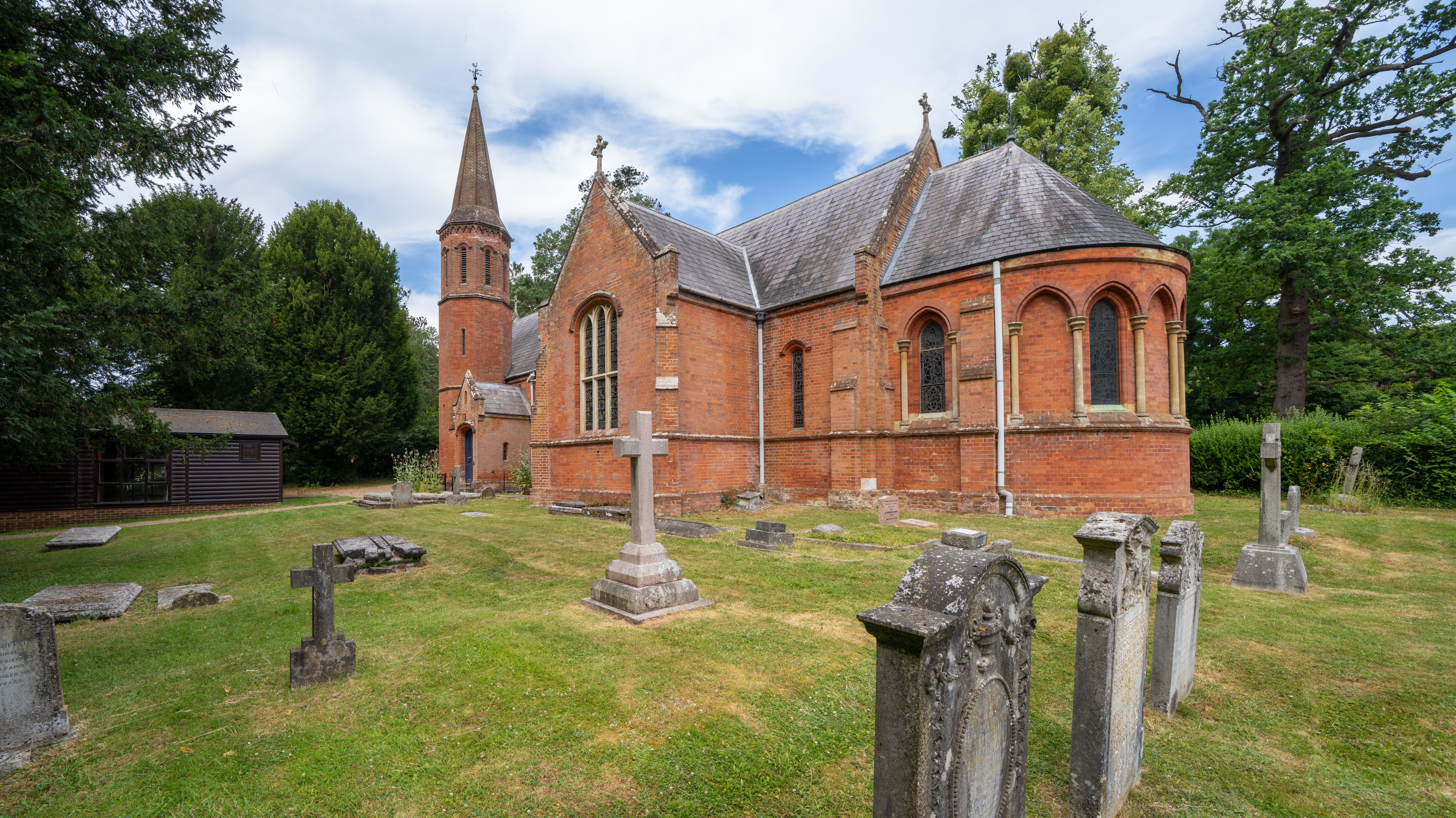 A picturesque brick church with a traditional cemetery in Latimer, England, surrounded by lush greenery.