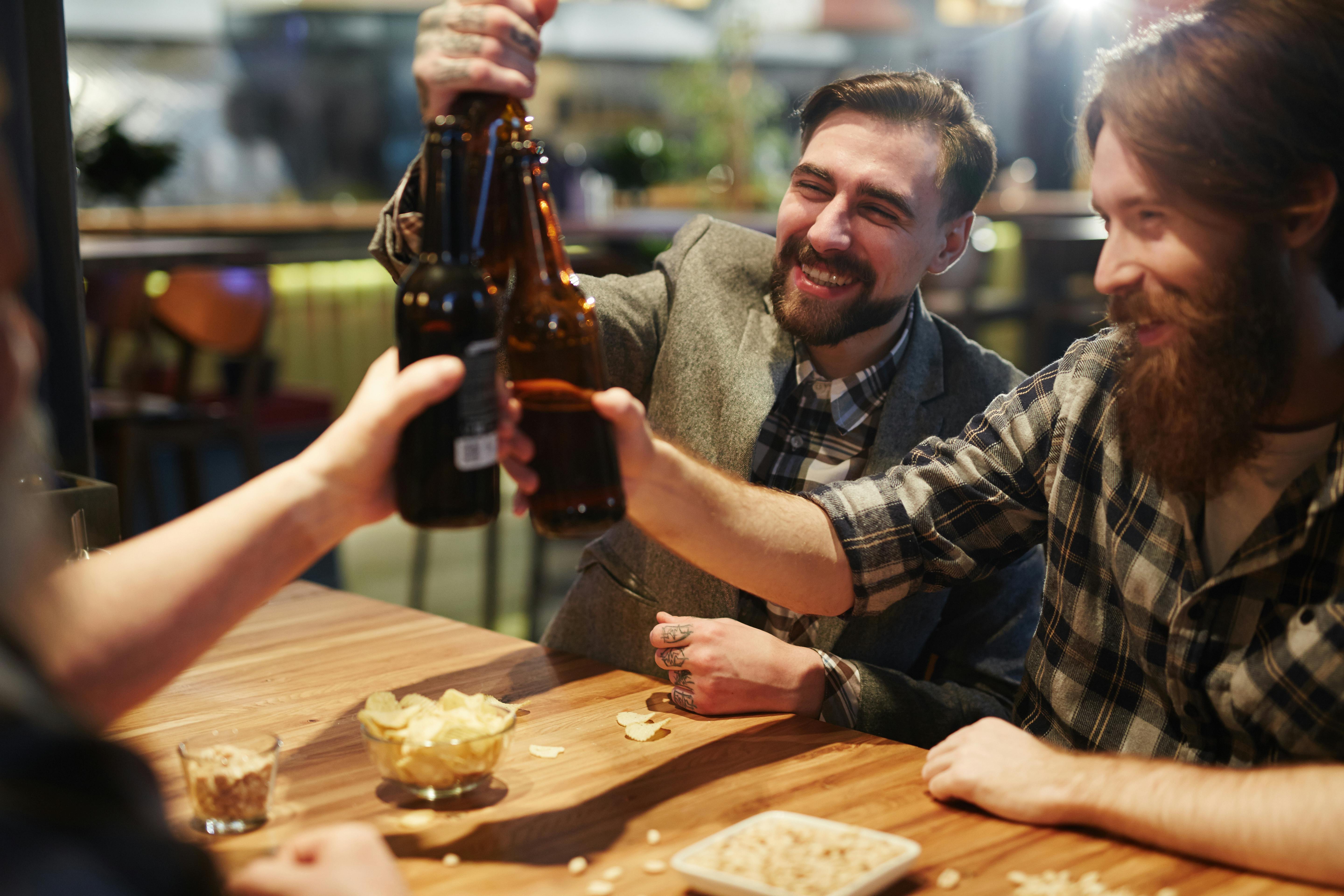Group of friends cheerfully toasting with beer bottles in a lively pub setting.