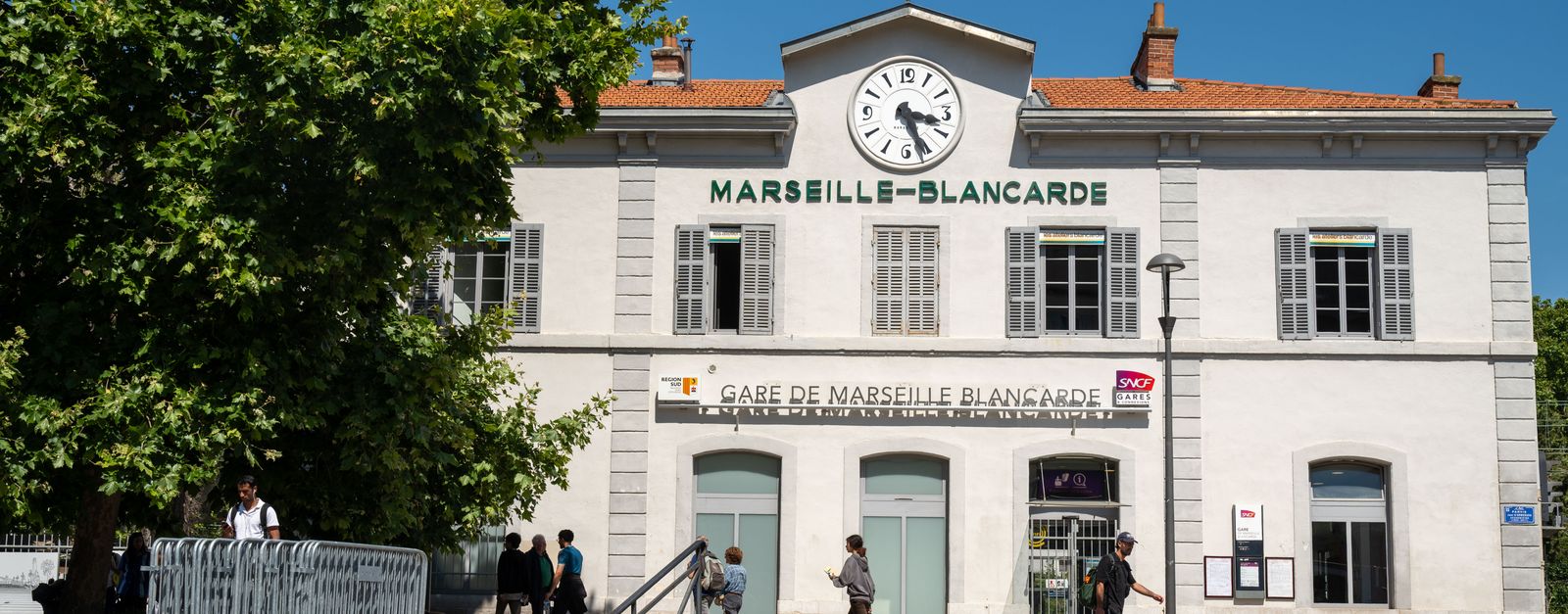 People walking in front of Gare de Marseille-Blancarde, a historic railway station in Marseille, France.