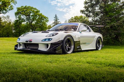 Free A sleek white sports car with spoiler parked on vibrant green grass under clear blue sky. Stock Photo