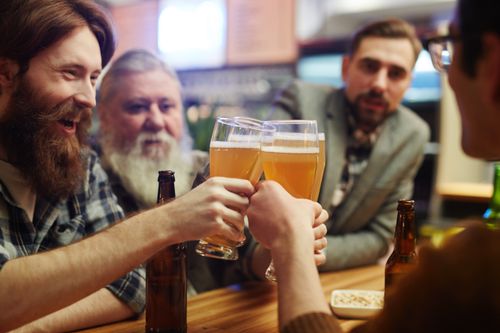Free Group of men enjoying beers and making a toast at a cozy pub setting. Captures camaraderie and leisure. Stock Photo