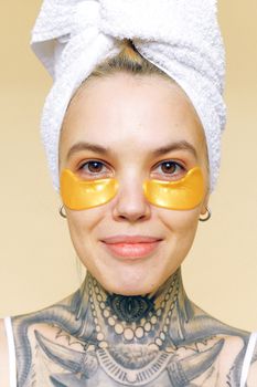 Portrait of a woman with golden eye patches and towel on head, embodying skincare and self-care.