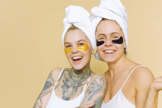 Two women enjoying a fun skincare routine with eye masks and towels on their heads.