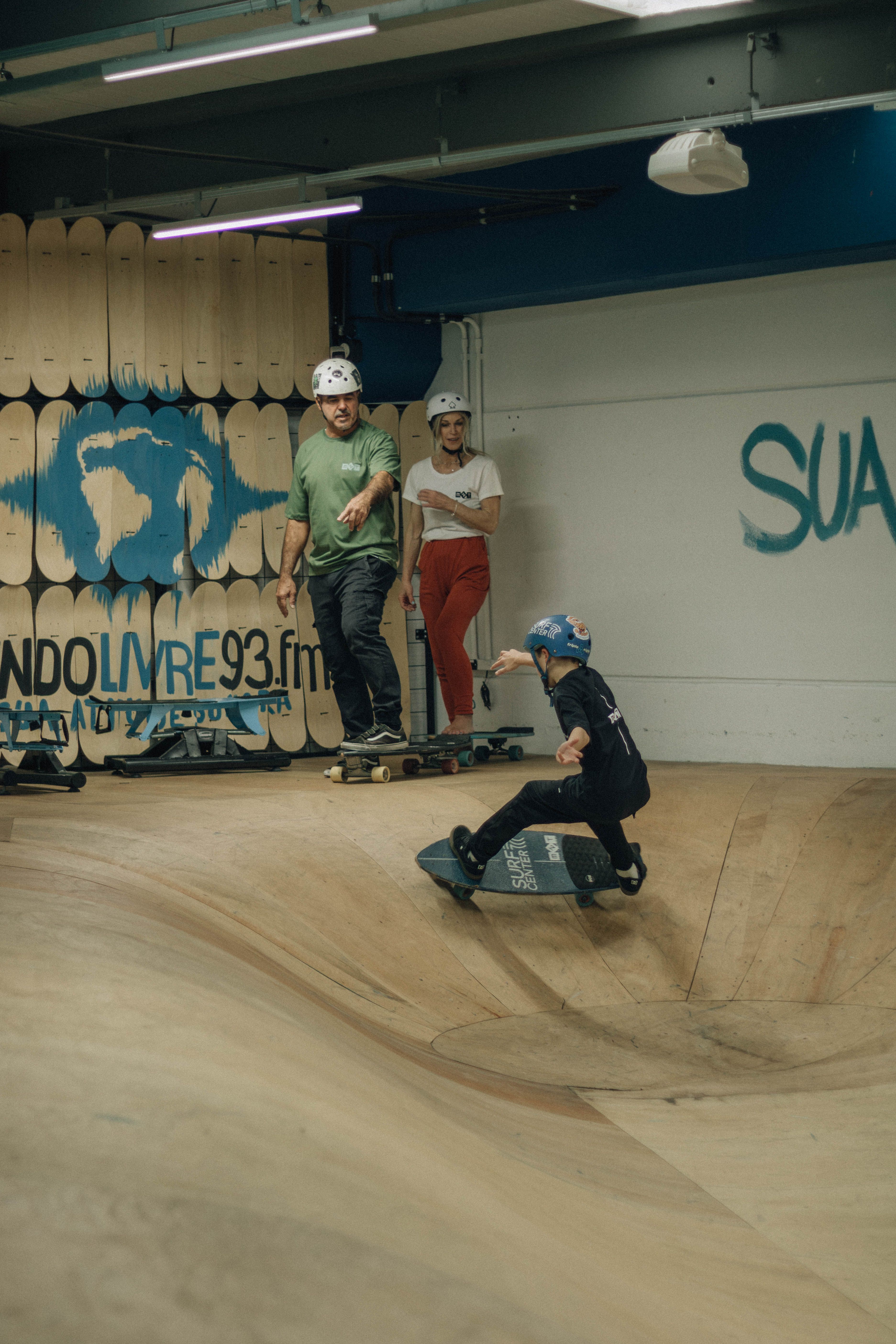 Young skateboarders practicing tricks in an indoor skate park under supervision.