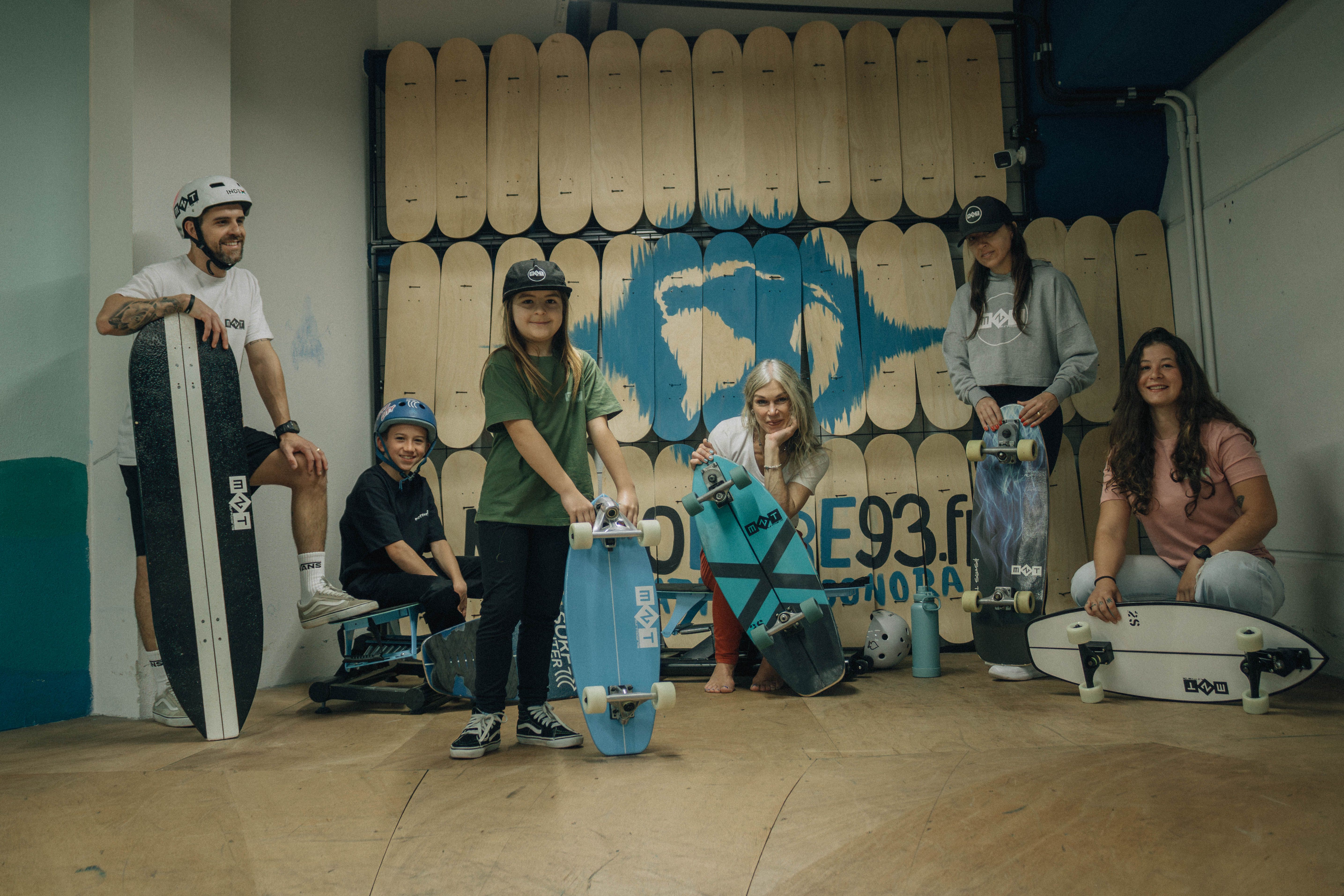 Adults and kids enjoying skateboarding indoors with various boards and gear.