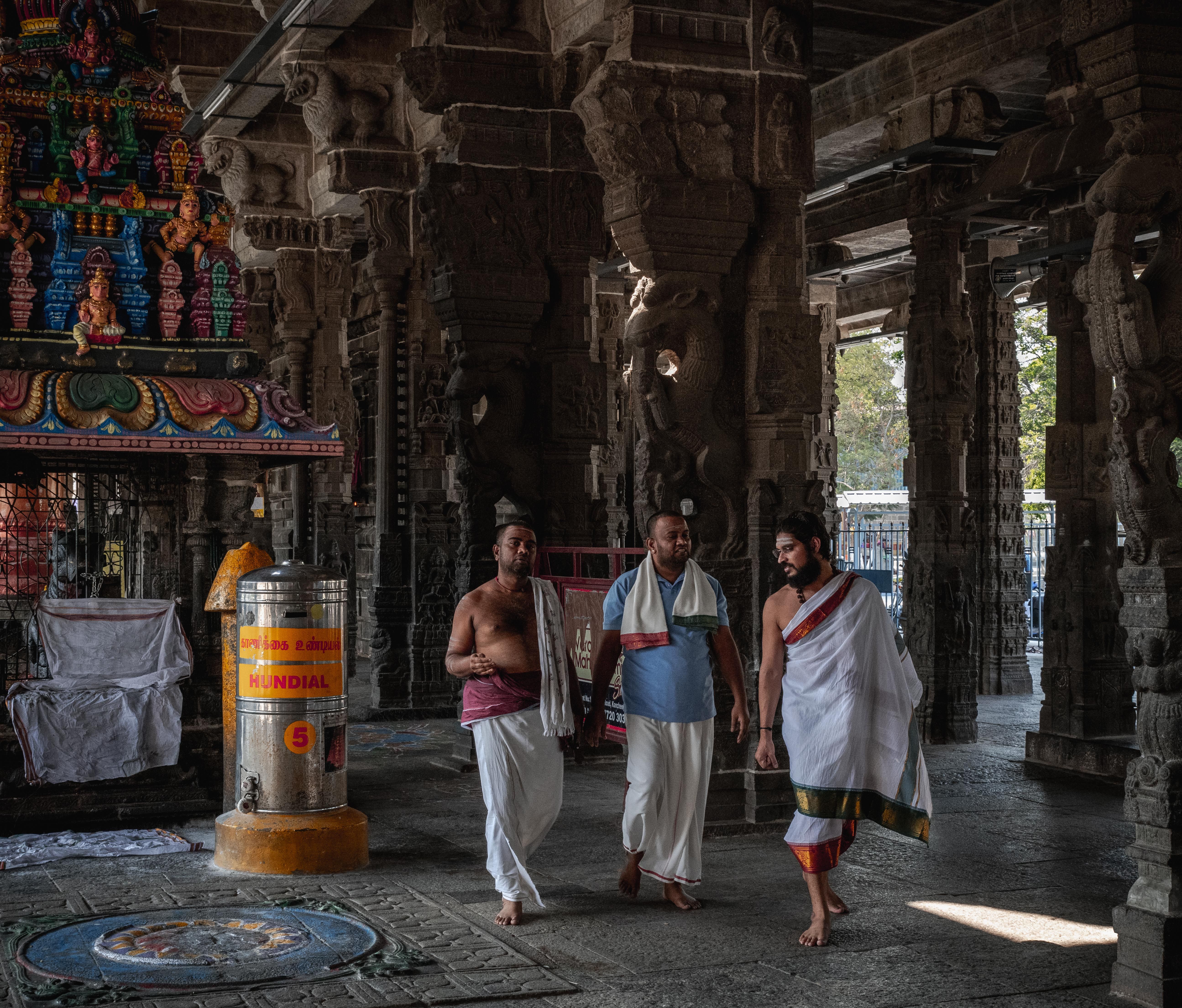 Three men in traditional attire walk through an ornate Hindu temple in Kanchipuram, India.
