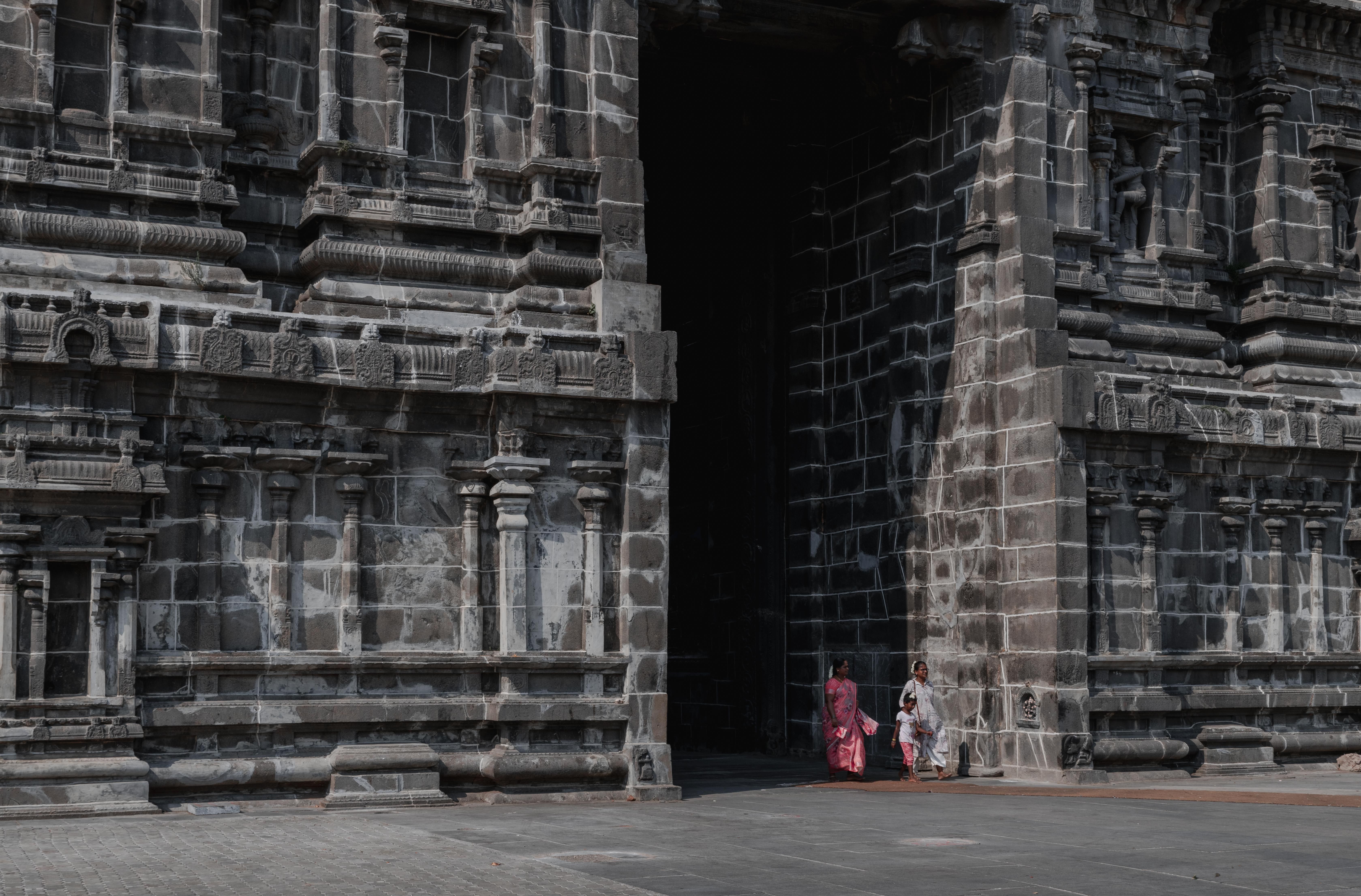 Intricate stone facade of temple in Kanchipuram with visitors passing by its entrance.