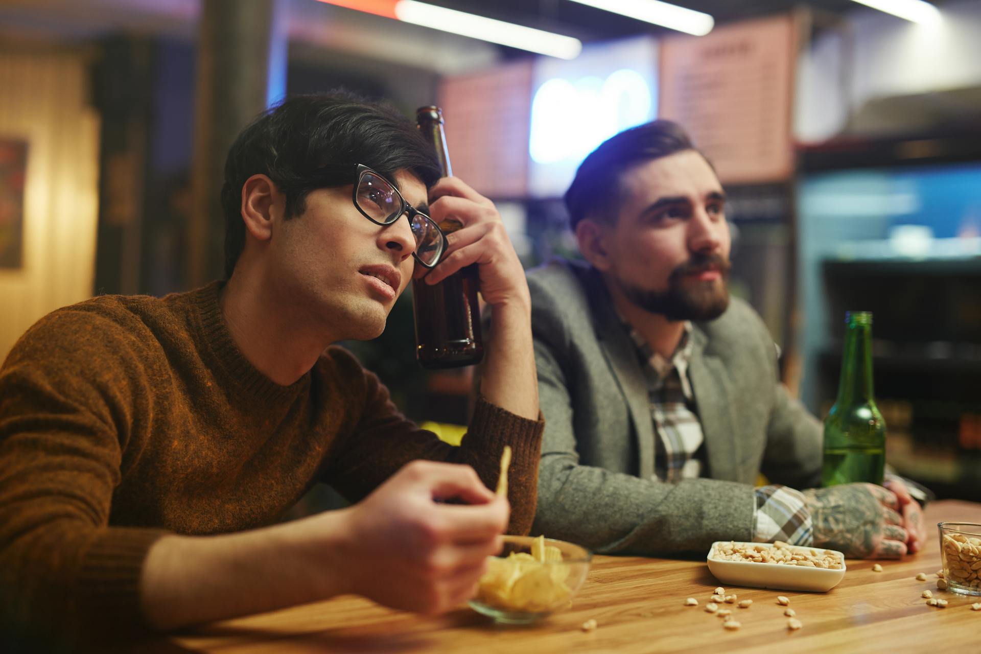 Two men watching sports with beers and snacks at a bar. Leisurely hangout.