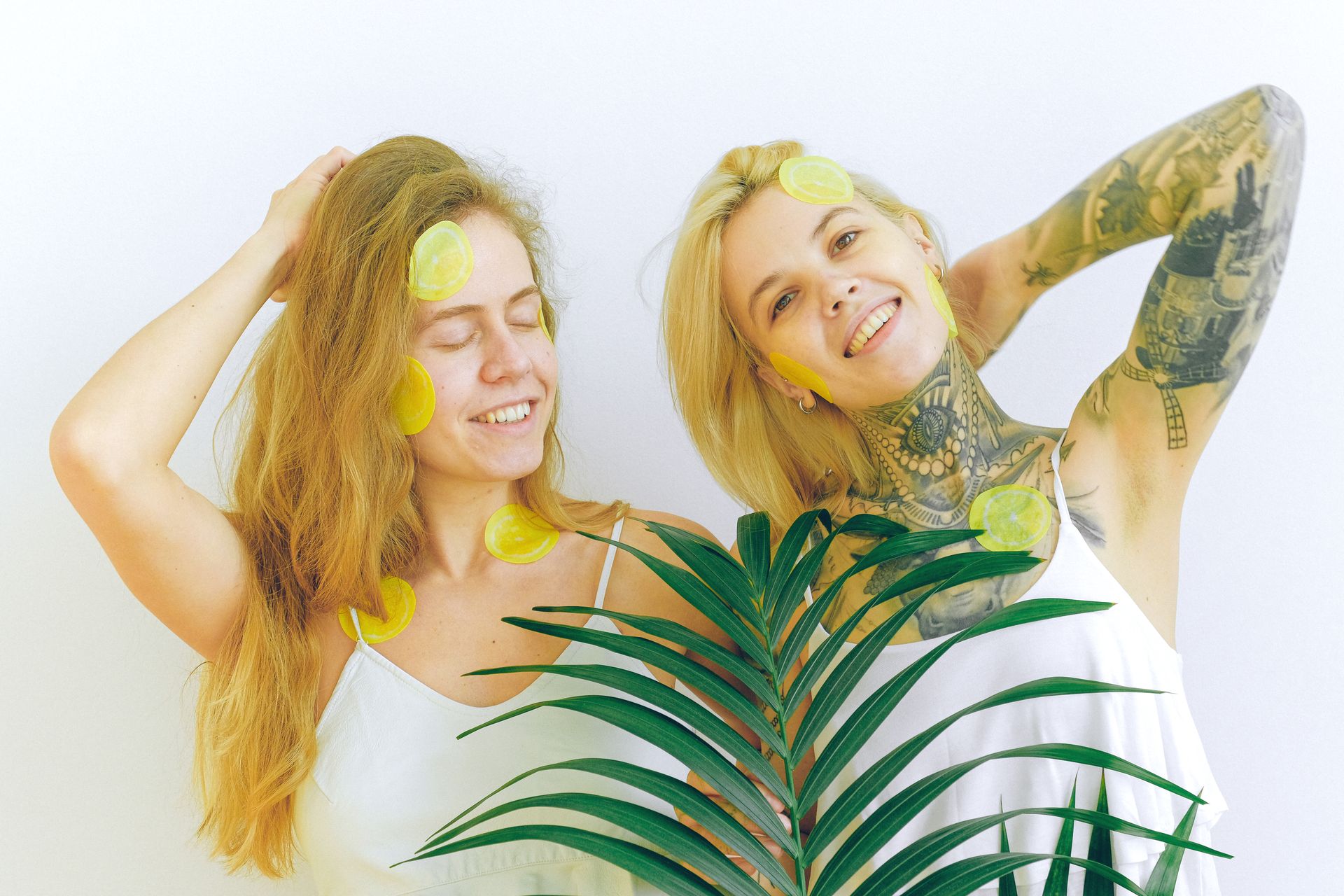 Two smiling women with lemon slices on their faces, enjoying a relaxing spa day with tropical leaves.
