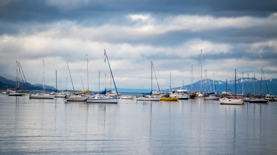 A serene view of sailboats anchored in Ushuaia, Argentina against a mountain backdrop.