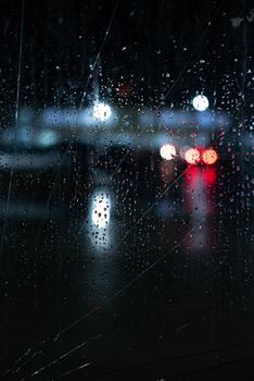 Raindrops on a window at night in Ushuaia, Argentina, with blurred city lights creating a moody scene.