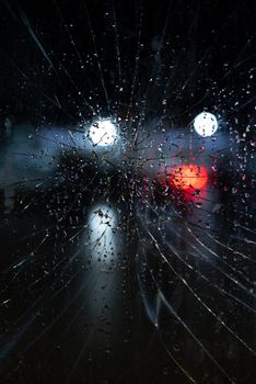 Dramatic view through cracked glass with raindrops, capturing night lights in Ushuaia, Argentina.