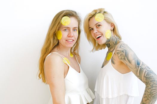 Smiling women having fun and laughing while staying together with slices of lemon patches on face during weekend in studio