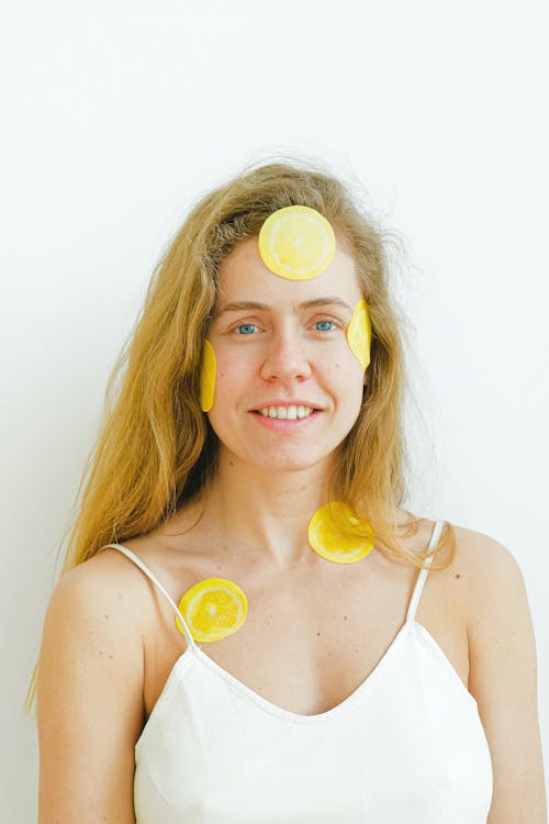 Optimistic female with slices of fresh lemon patches on face smiling and looking at camera while having skincare procedure during weekend