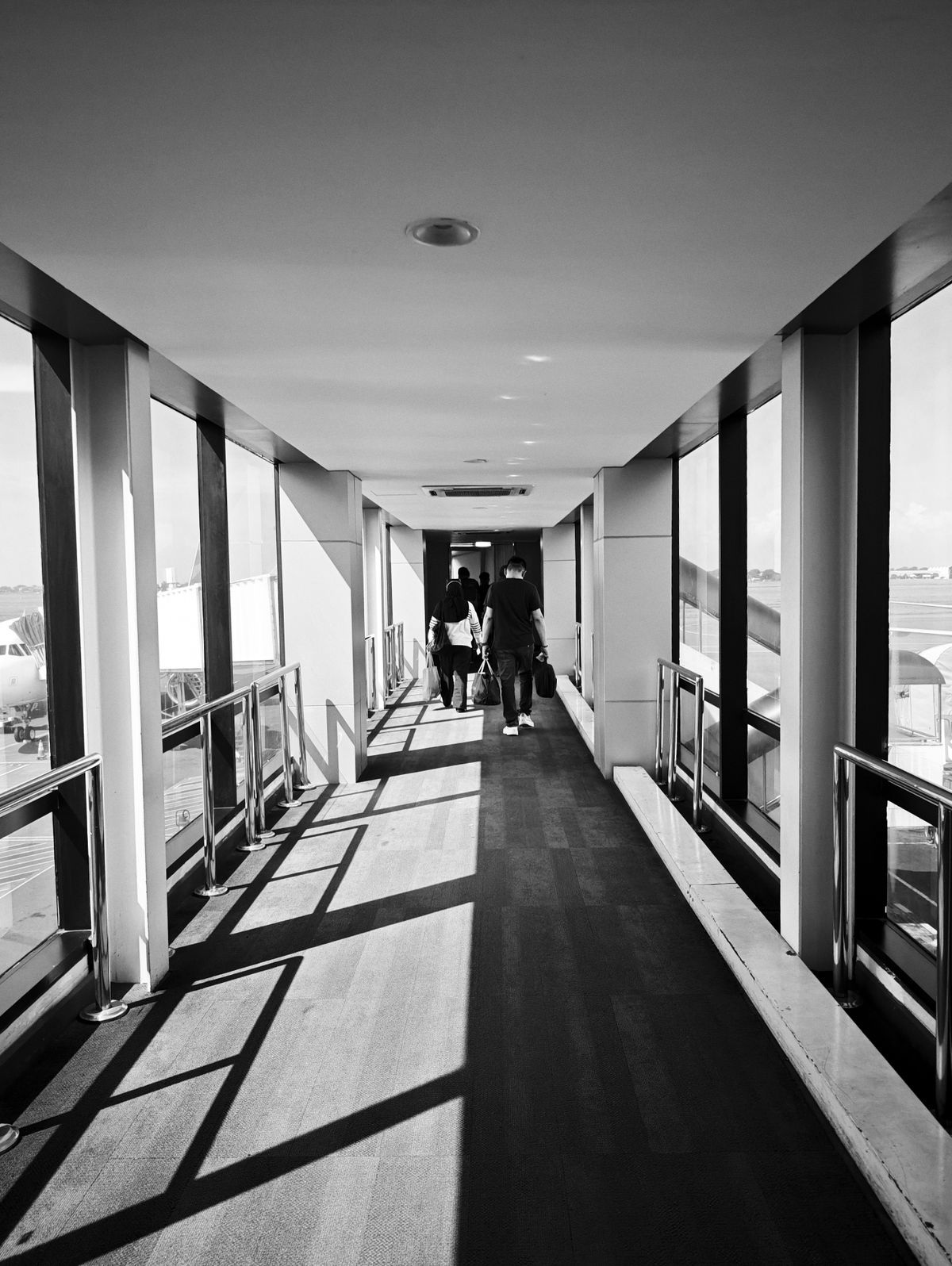 Travellers walking through an airport jet bridge towards their gate