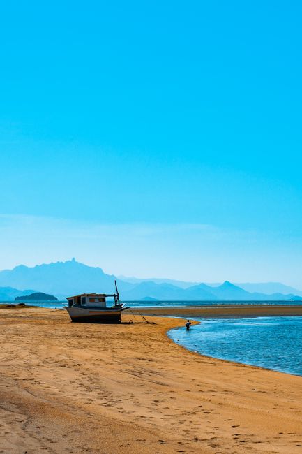 Serene beach with a boat and a person walking, under a clear blue sky.