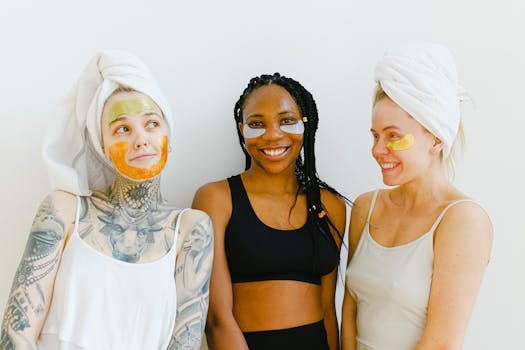 Three diverse women with face masks and towels smiling indoors, embracing wellness.