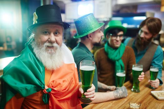 Group of friends celebrating Saint Patrick's Day with green beer at a pub.