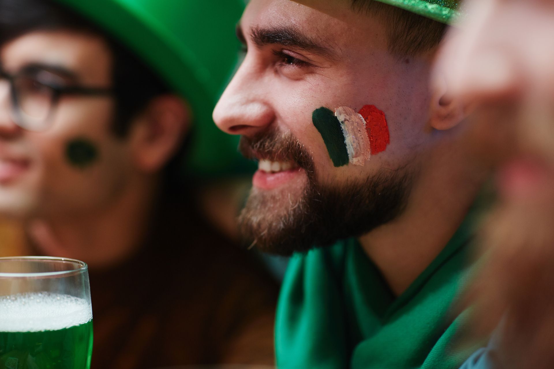 Smiling group of friends celebrating St. Patrick's Day with face paint and green drinks.