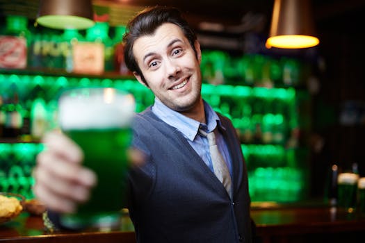 Smiling man holding a green beer celebrating in an atmospheric bar setting.