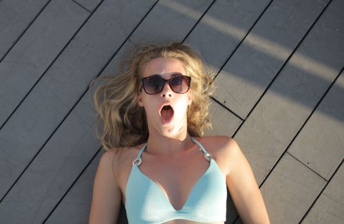 Free Blonde woman in sunglasses lying outdoors on a wooden deck, looking surprised. Stock Photo