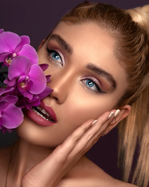 Close -up Photo of Woman With Pink Lipstick Holding Purple Flowers