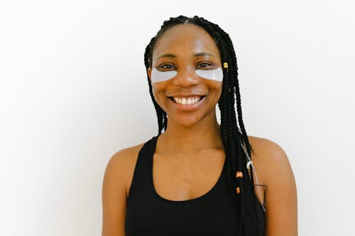 African American woman with braided hair and eye patches smiling in a studio setting.