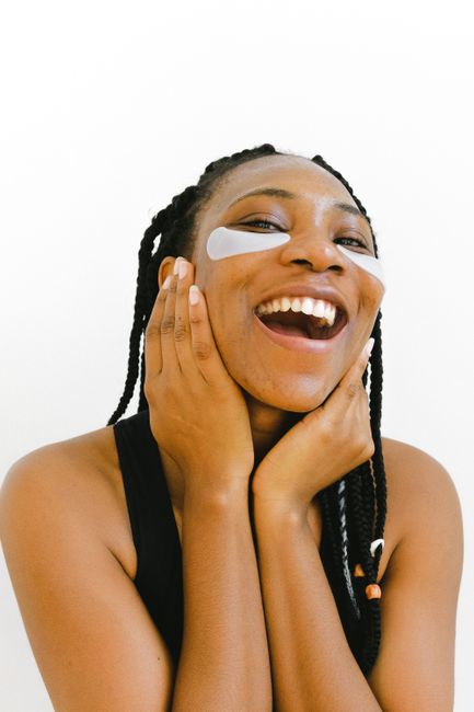 Cheerful African American female with white eye patches for skin care on face laughing and looking at camera
