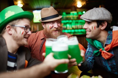 Free Three men enjoy St. Patrick's Day in a pub, clinking glasses of green beer. Stock Photo
