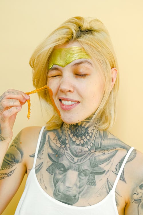 Young tattooed woman pulling off facial mask