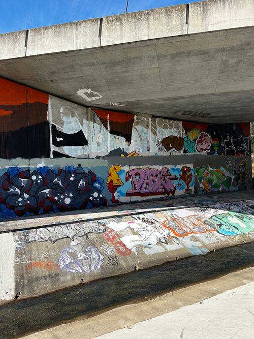 Free Colorful graffiti art displayed on a concrete wall under a bridge, showcasing urban creativity. Stock Photo