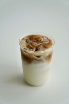A delicious iced coffee with milk served in a clear glass on a white backdrop.