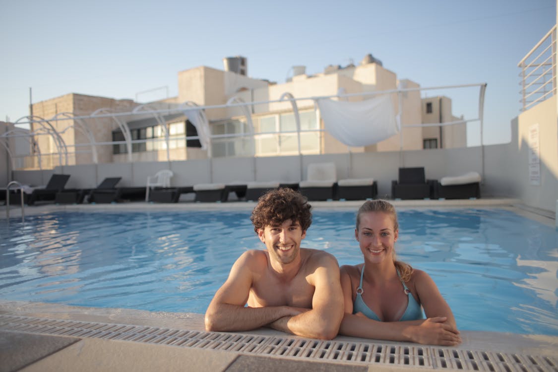 Topless Man Sitting on Swimming Pool Besides a Lady in Blue Bikini