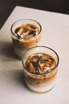 Top view of two iced coffee drinks in glass cups on a light-colored table.