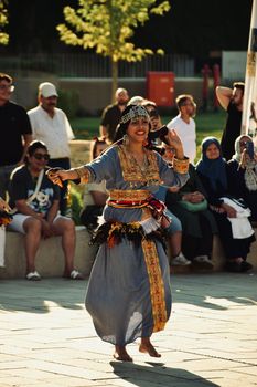 A woman in traditional attire performs a cultural dance outdoors in front of an audience.