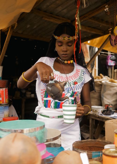 Free A woman in traditional attire pours a beverage at a lively market setting. Stock Photo