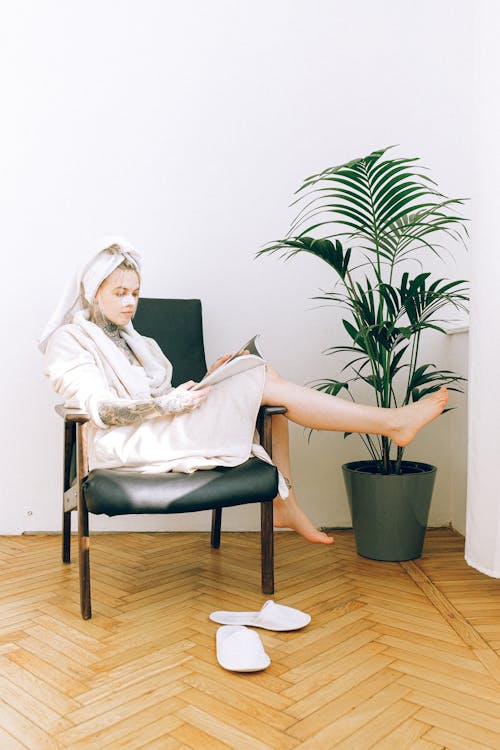 Woman in robe and cosmetic mask reading magazine