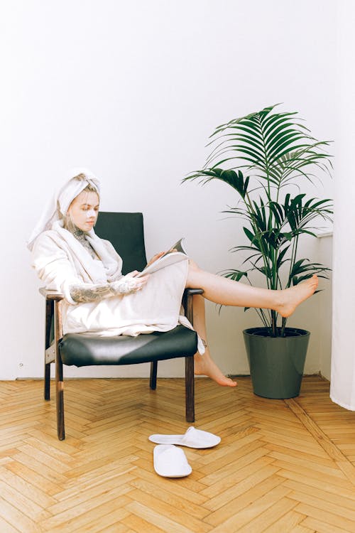 Woman in robe and cosmetic mask reading magazine Better Skin - While Working from Home