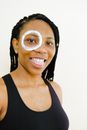 Happy African American lady in black wear with lotion circle around one eye showing tongue and looking at camera while standing on white background
