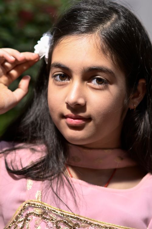 Free A young girl with long dark hair in a pink dress, holding a white flower in her hair. Stock Photo