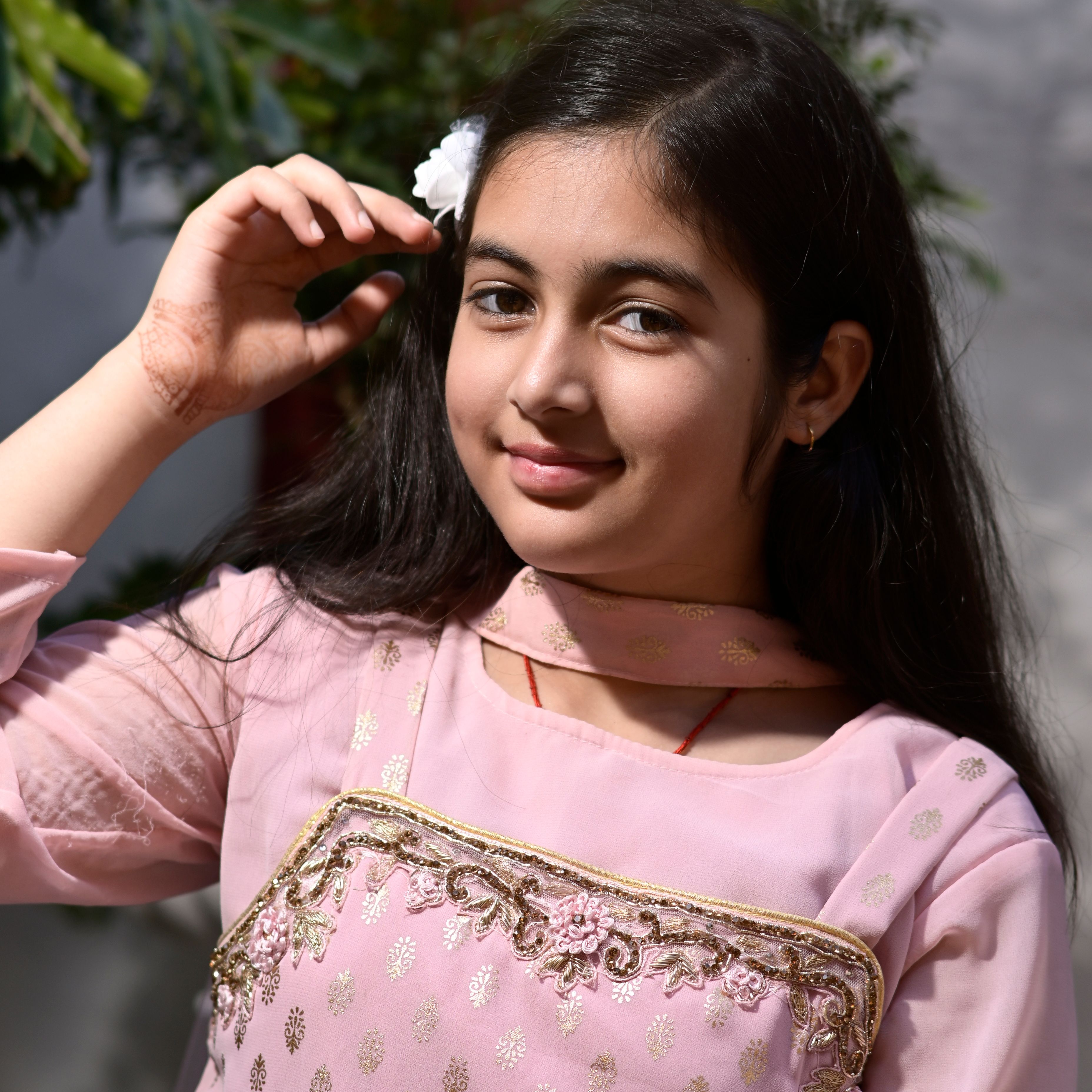 Smiling girl in pink traditional dress posing outdoors with floral hair accessory.