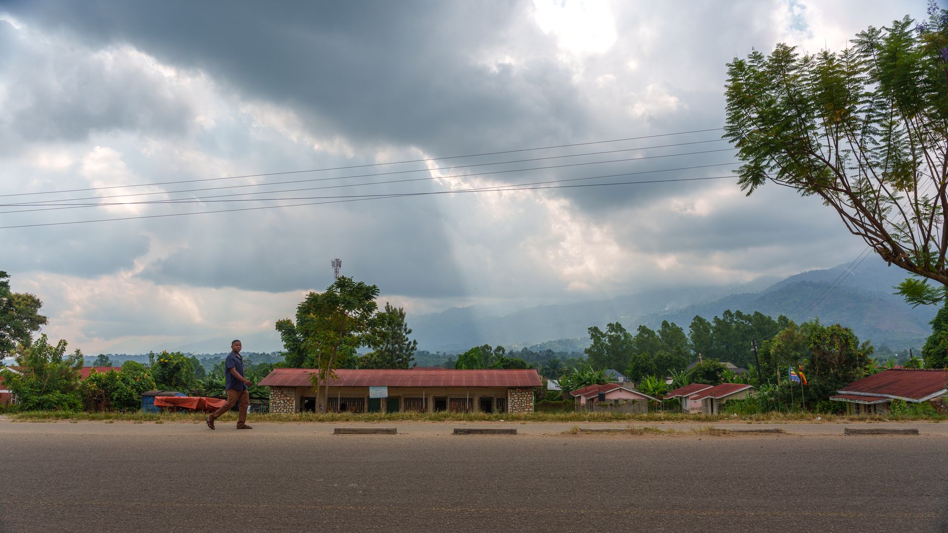 A serene rural scene in Uganda featuring a road, houses, and dramatic cloudy skies.
