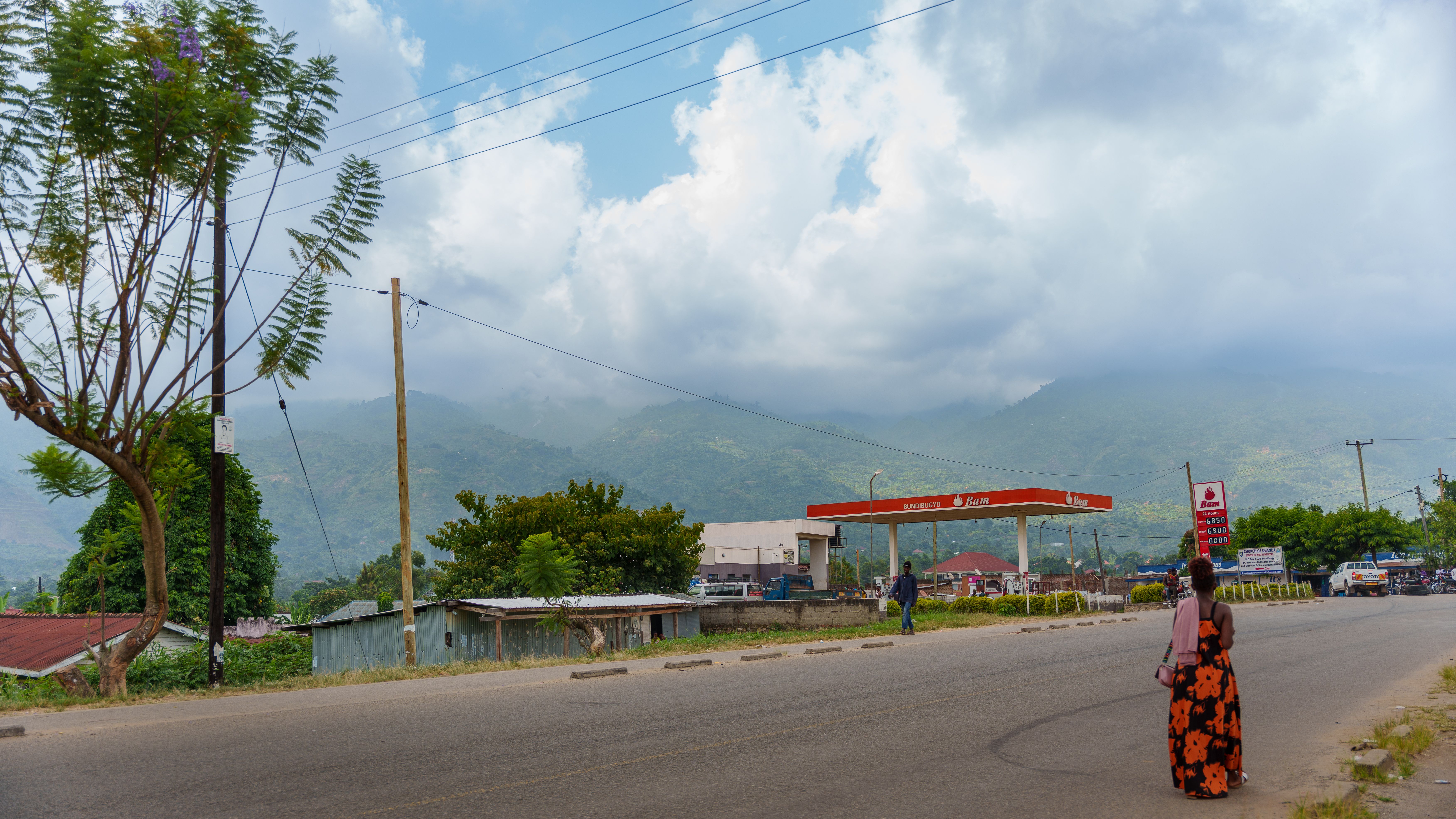 A tranquil roadside scene in Uganda with mountains, a gas station, and a lone pedestrian.
