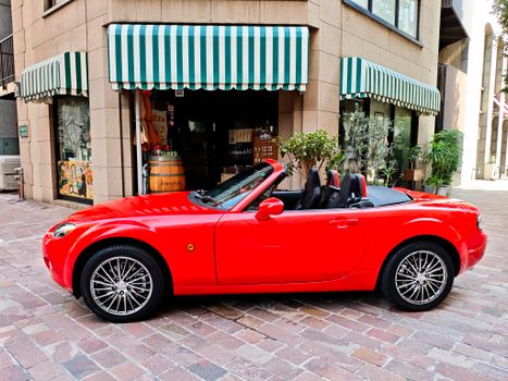 Eye-catching red convertible car parked outside a charming cafe with striped awnings.
