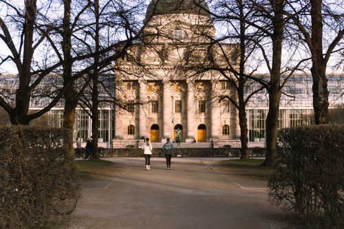 Free A stunning building in Munich's garden, captured at dusk with bare trees framing the path. Stock Photo
