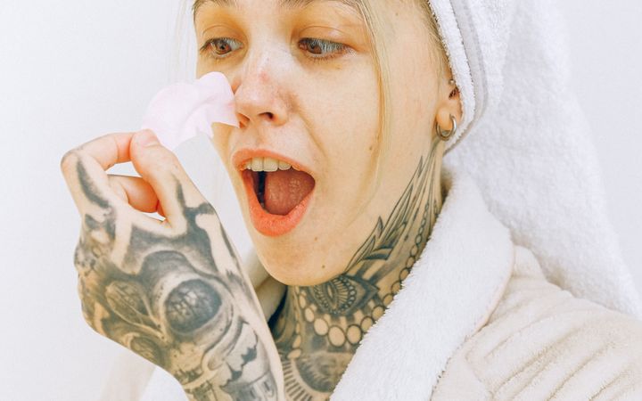 Tattooed woman enjoying a skincare routine with a pore strip in a cozy robe and towel wrap.