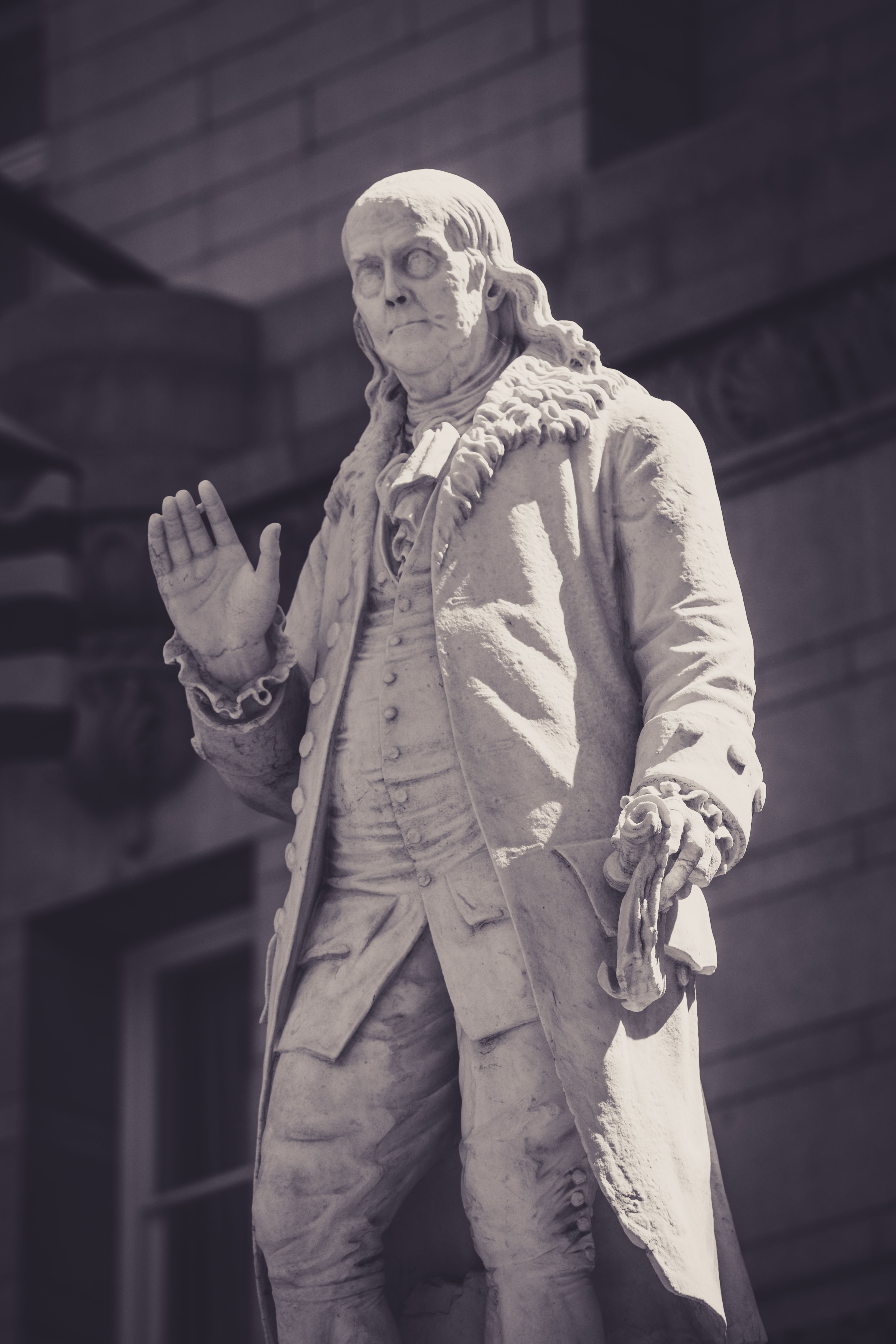 Sepia-toned image of Benjamin Franklin statue against an urban backdrop.