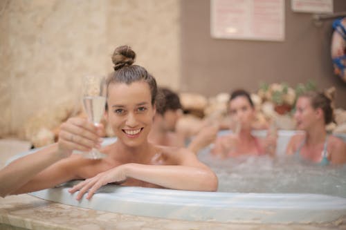 Cheerful friends with glass of champagne sitting in jacuzzi