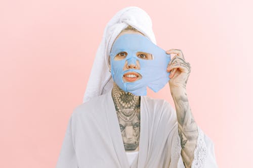 Woman with tattoos removing collagen mask from face
